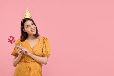 Photo of Happy young woman in party hat with candy on pink background