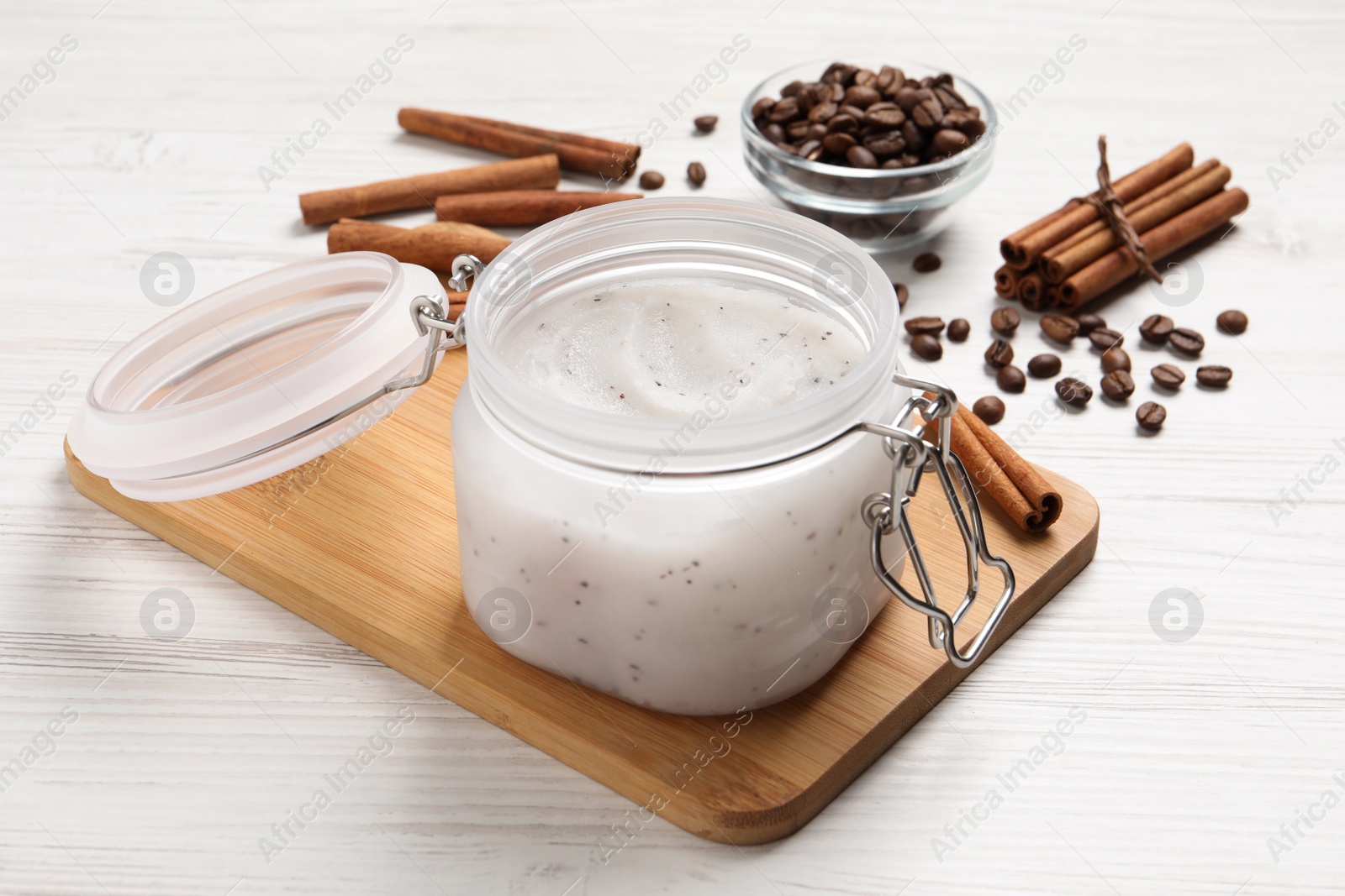 Photo of Body scrub in glass jar, cinnamon and coffee beans on white wooden table