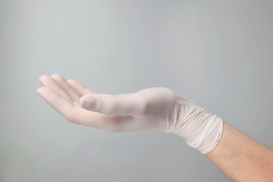 Doctor wearing white medical glove holding something on grey background, closeup