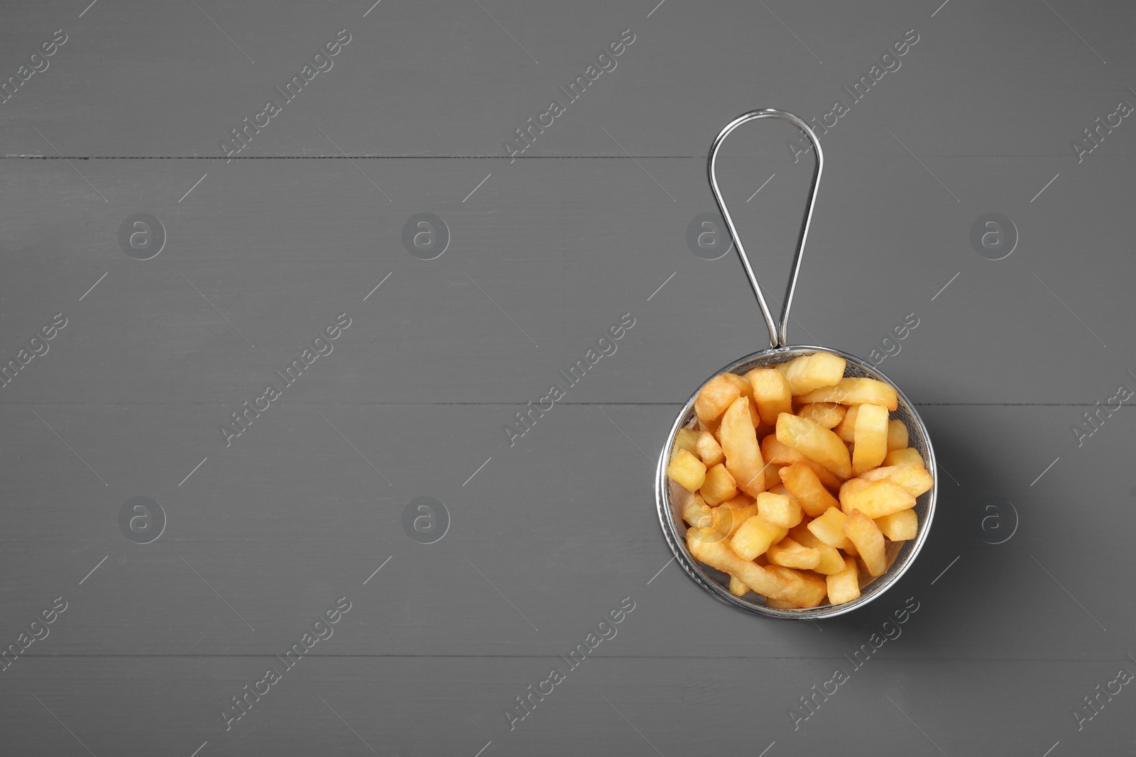 Photo of Metal basket with tasty French fries on grey wooden table, top view. Space for text