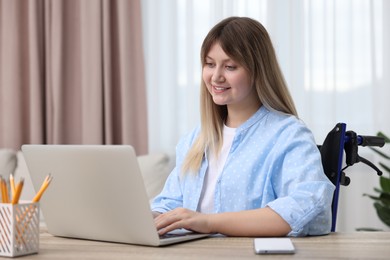 Woman in wheelchair using laptop at home