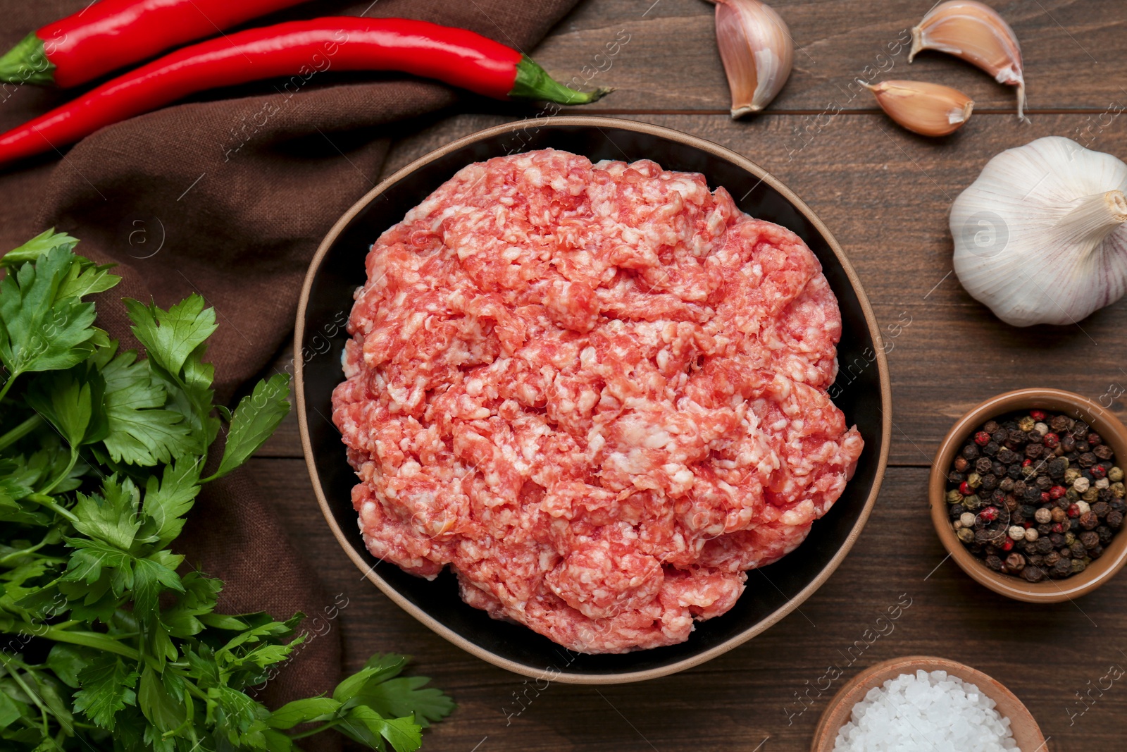 Photo of Bowl of raw fresh minced meat and ingredients on wooden table, flat lay