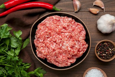 Bowl of raw fresh minced meat and ingredients on wooden table, flat lay