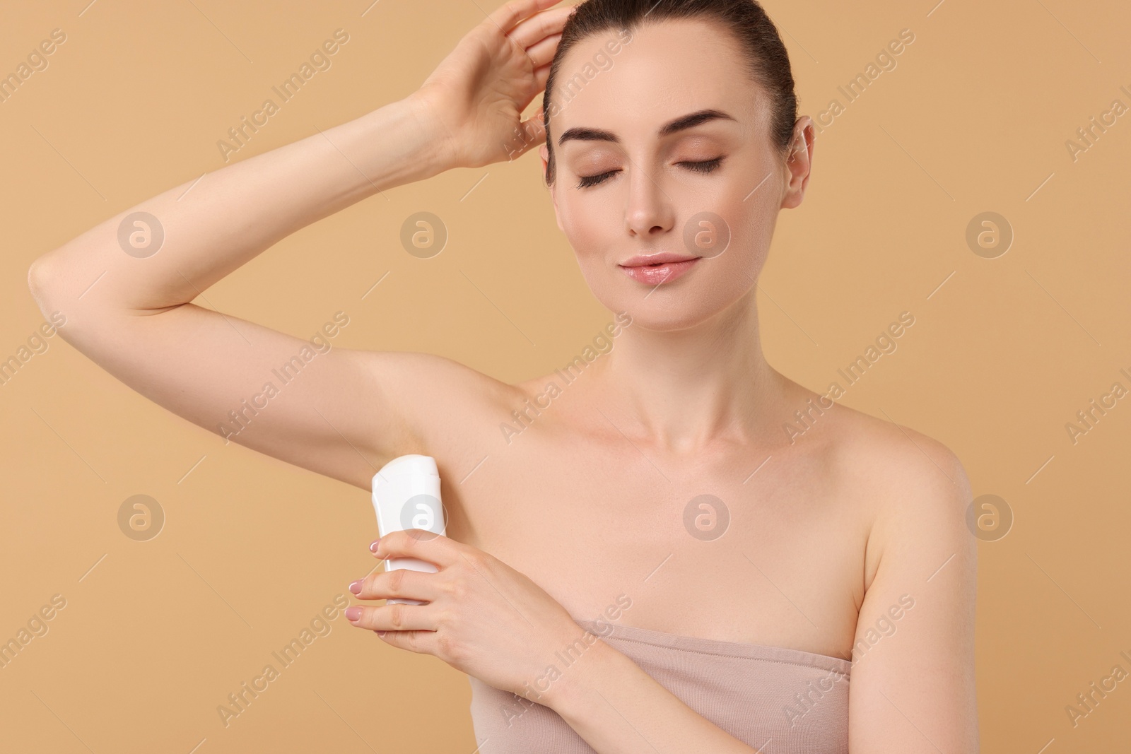 Photo of Beautiful woman applying deodorant on beige background