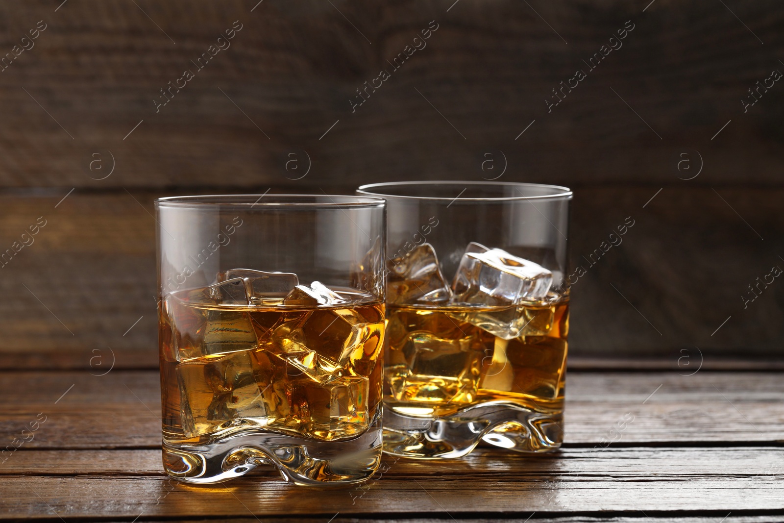Photo of Whiskey with ice cubes in glasses on wooden table, closeup