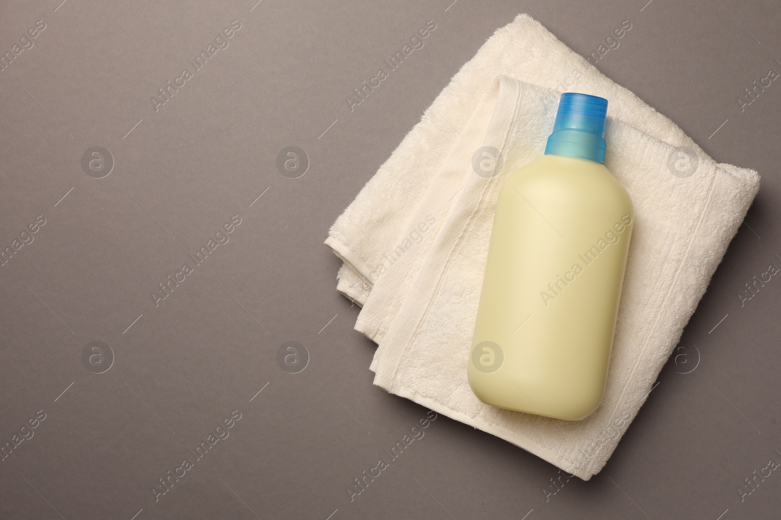 Bottle of fabric softener and terry towel on gray background, top view. Space for text Photo of Bottle of fabric softener and terry towel on gray background, top view. Space for text