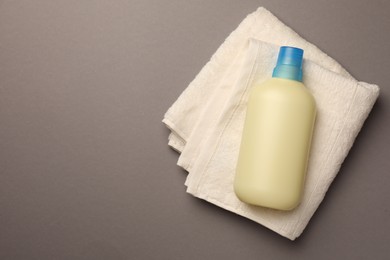 Photo of Bottle of fabric softener and terry towel on gray background, top view. Space for text