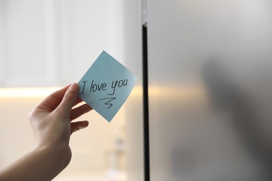 Woman with sticky note saying I Love You near fridge door, closeup. Romantic message