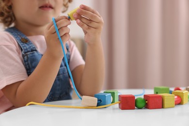 Photo of Motor skills development. Little girl playing with wooden pieces and string for threading activity at table indoors, closeup