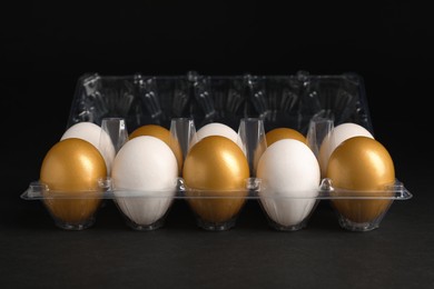 Photo of Golden and ordinary chicken eggs in plastic box on black background