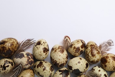 Photo of Speckled quail eggs and feathers on white background, flat lay. Space for text