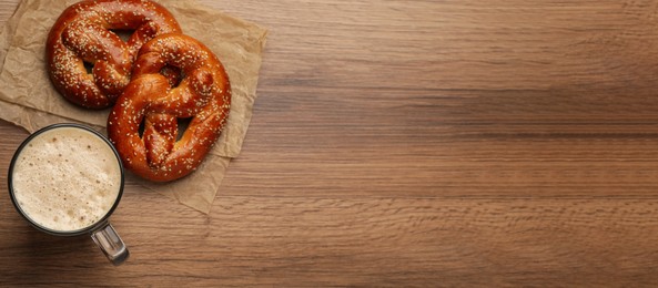 Image of Tasty pretzels and glass of beer on wooden table, flat lay with space for text. Banner design