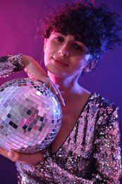 Photo of Beautiful young woman with disco ball posing on color background in neon lights