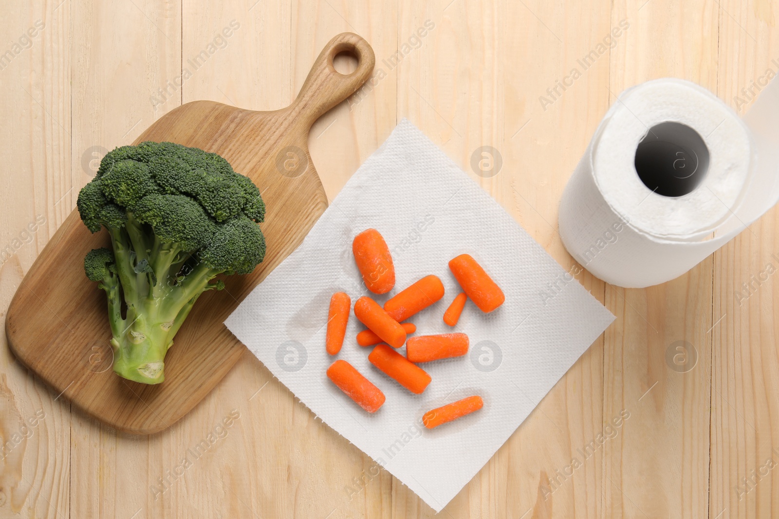 Photo of Carrots drying on paper towel and broccoli on wooden table, flat lay