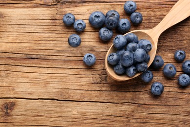 Photo of Spoon with tasty fresh blueberries on wooden table, flat lay. Space for text