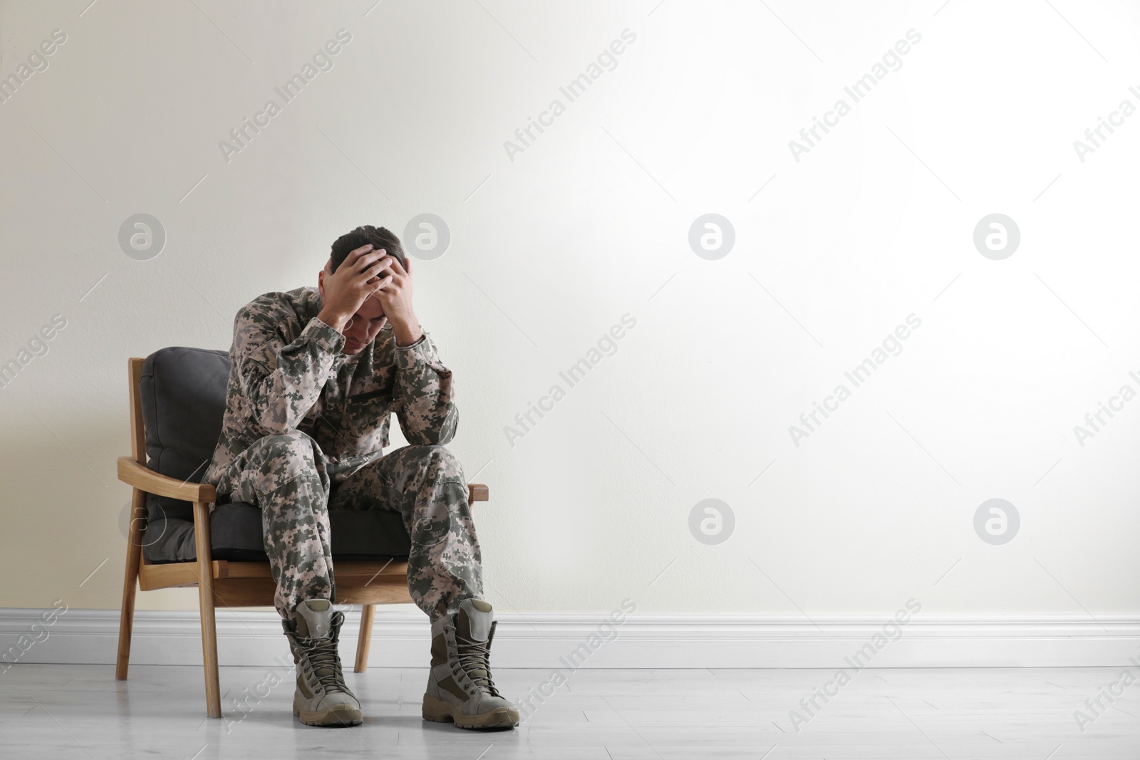 Photo of Stressed military officer sitting in armchair near white wall indoors. Space for text