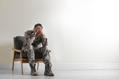 Stressed military officer sitting in armchair near white wall indoors. Space for text