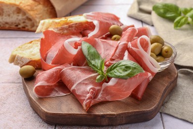 Photo of Slices of tasty cured ham, olives, bread and basil on tiled table, closeup