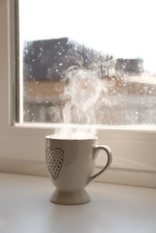 Photo of Cup of hot drink near window on rainy day. Space for text