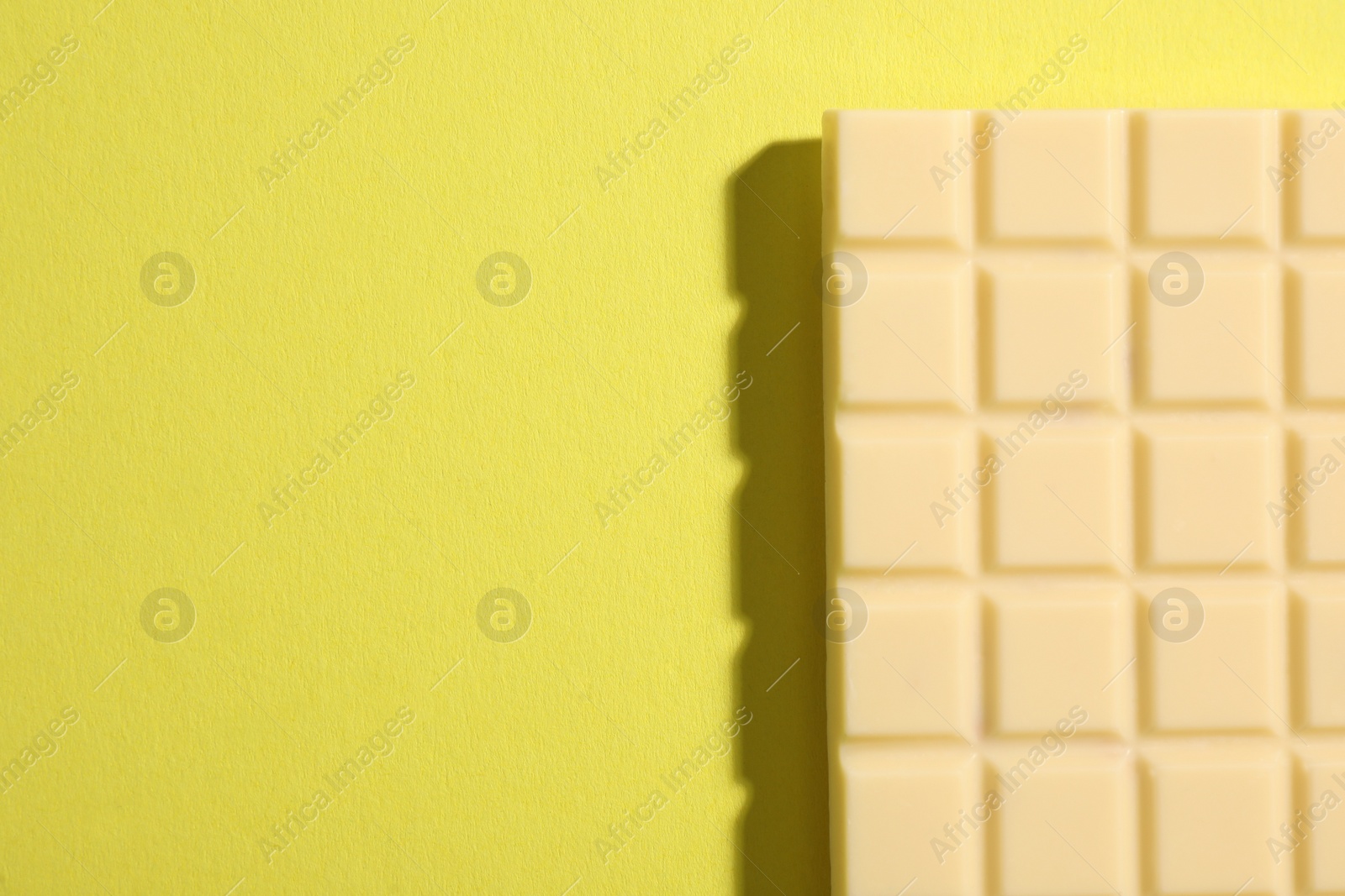 Photo of Delicious white chocolate bar on yellow background, top view. Space for text