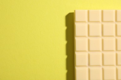 Photo of Delicious white chocolate bar on yellow background, top view. Space for text