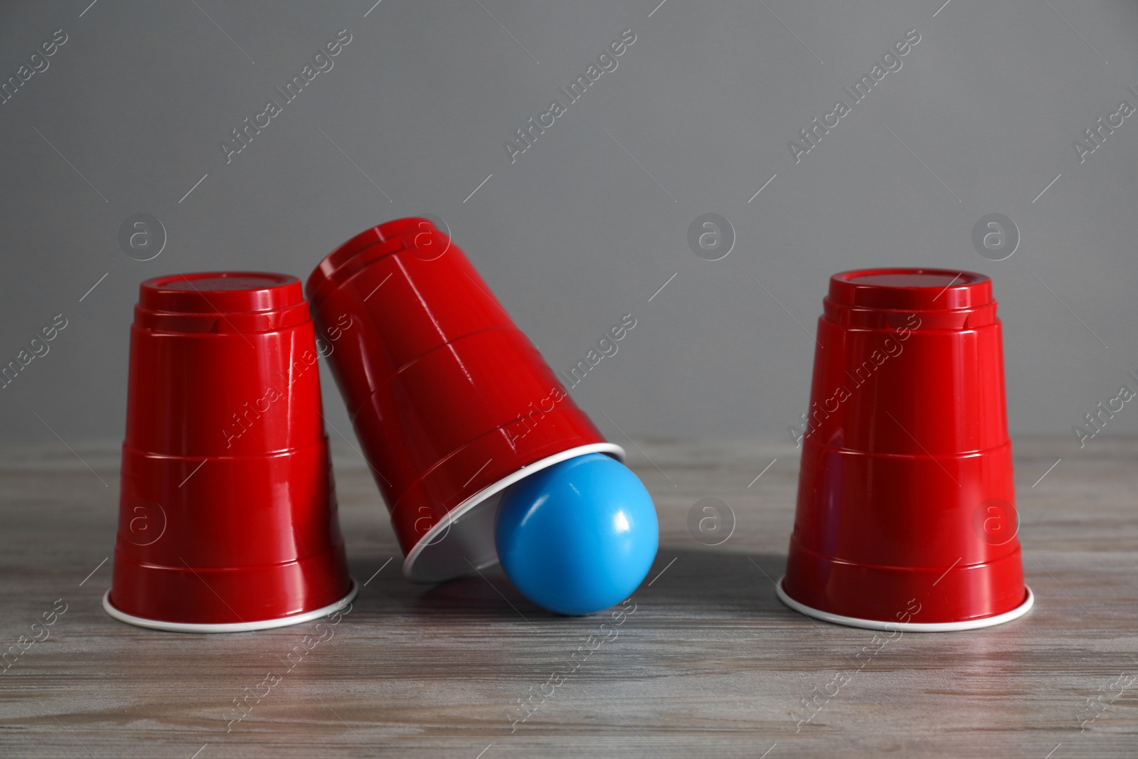 Photo of Shell game. Three red cups and ball on wooden table