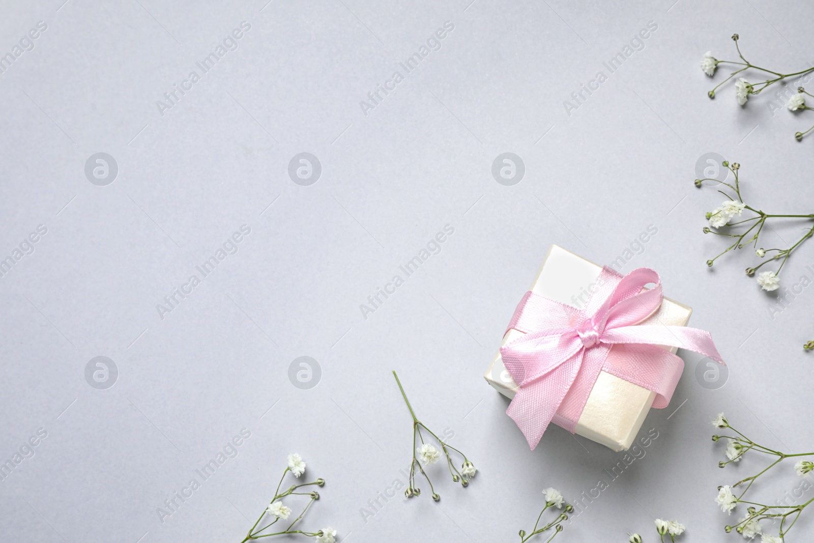 Photo of Flat lay composition with flowers and gift on light grey background, space for text. Happy Mother's day