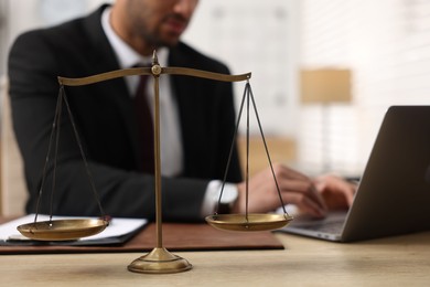 Photo of Lawyer working with laptop at table in office, focus on scales of justice