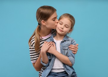 Photo of Young woman kissing her little daughter on light blue background. Happy Mother's Day