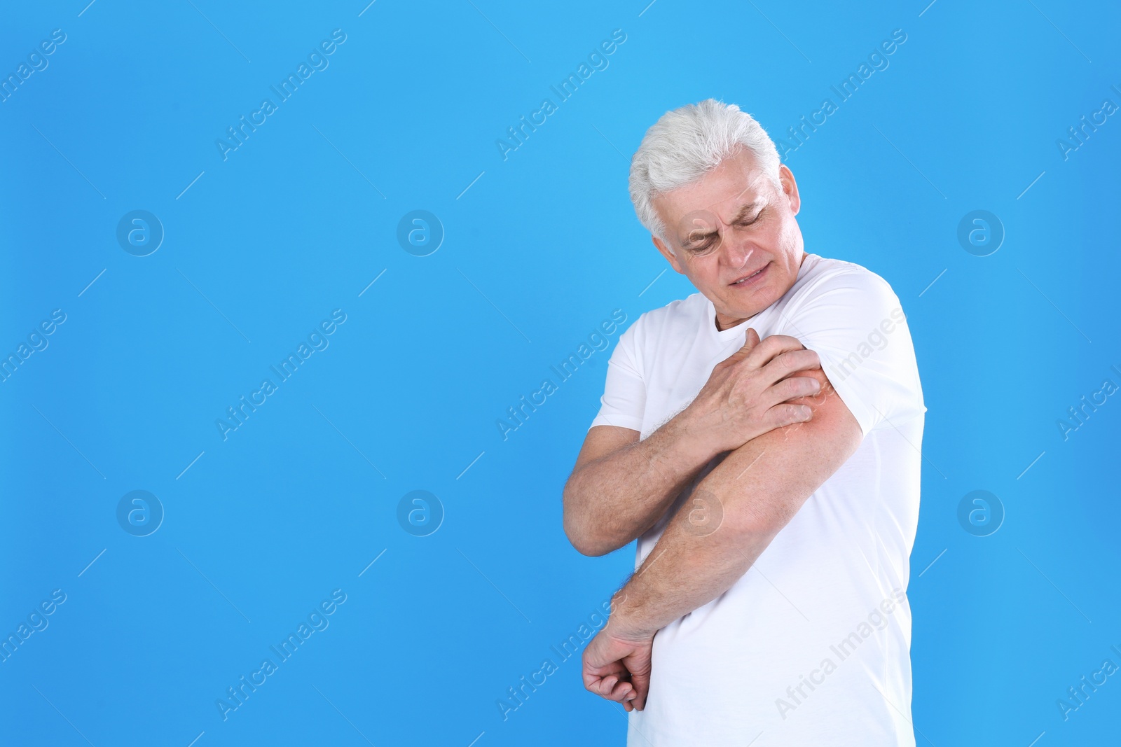 Photo of Senior man scratching arm on color background, space for text. Allergy symptom