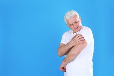 Senior man scratching arm on color background, space for text. Allergy symptom