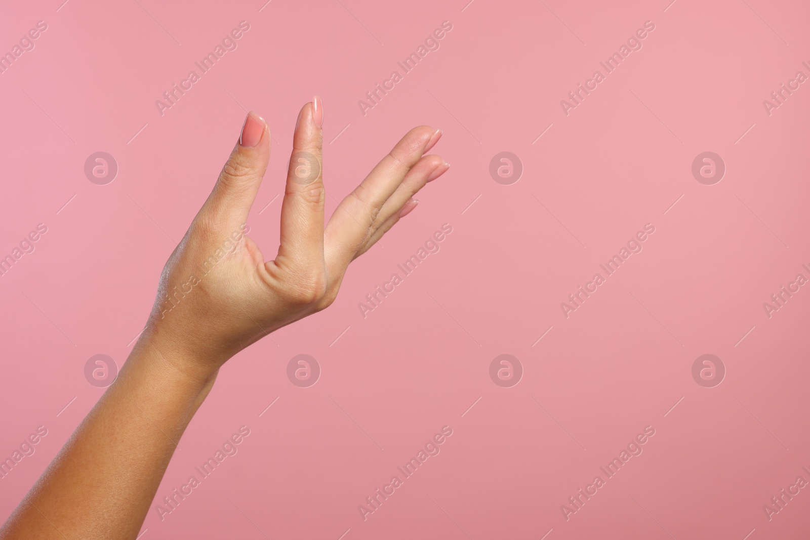 Photo of Woman holding something in fingers on pink background, closeup. Space for text