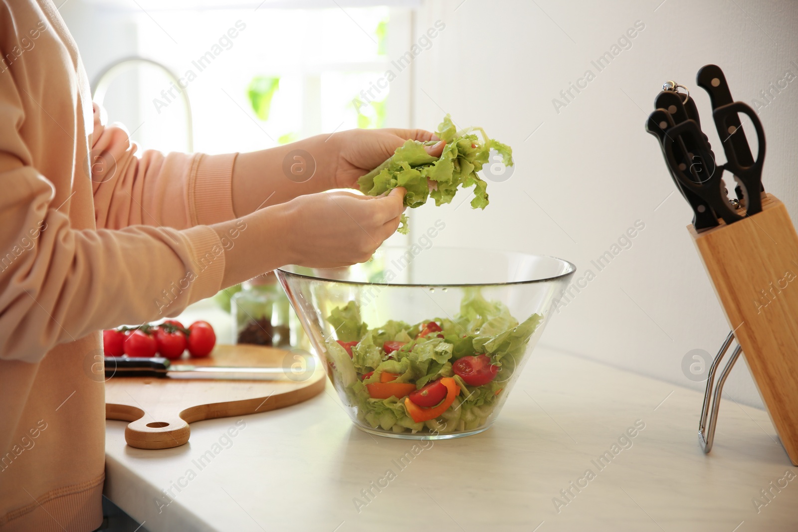 Photo of Young woman cooking salad at table in kitchen, closeup