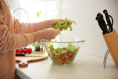 Young woman cooking salad at table in kitchen, closeup