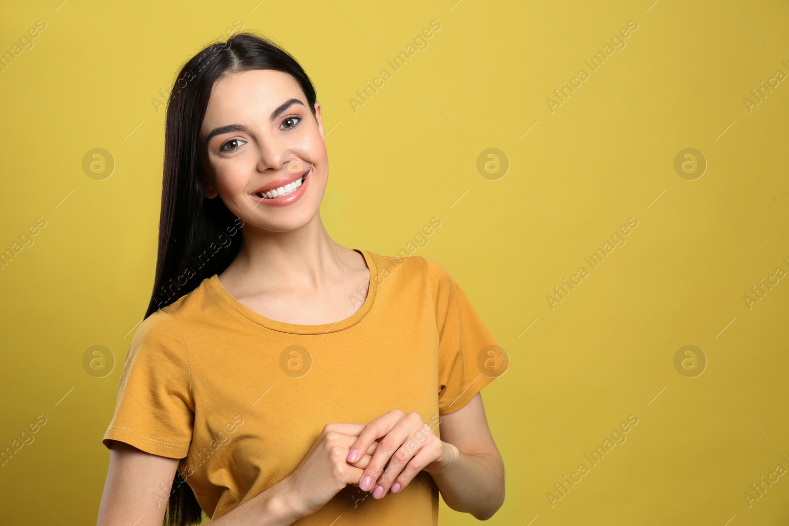 Photo of Portrait of happy young woman with beautiful black hair and charming smile on yellow background, space for text