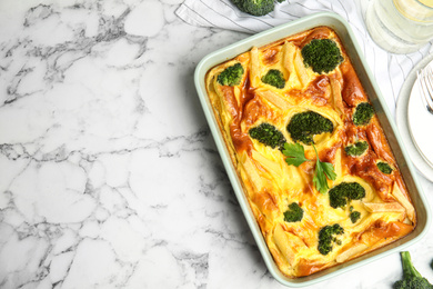 Tasty broccoli casserole in baking dish on white marble table, flat lay. Space for text