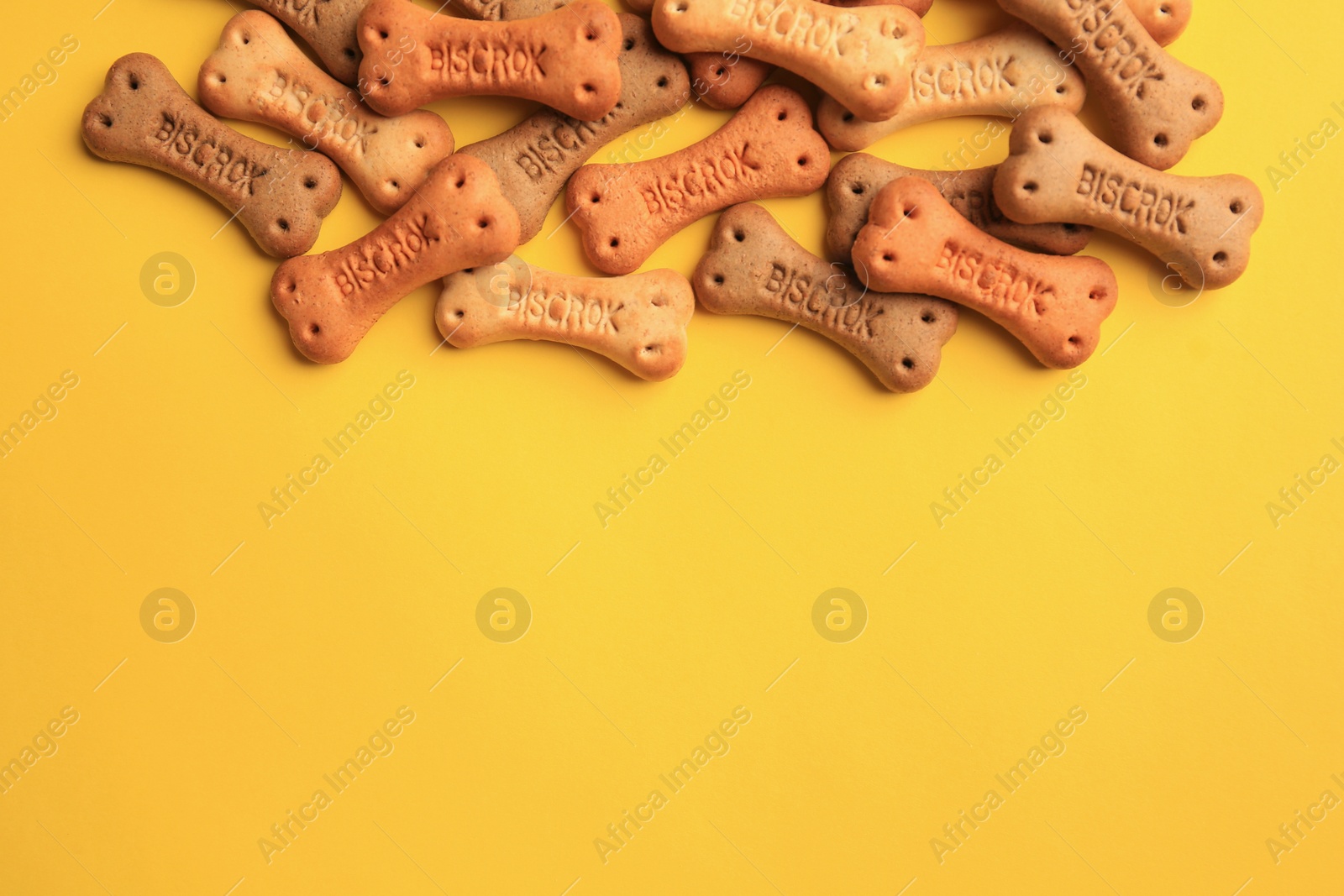 Photo of Bone shaped dog cookies on yellow background, flat lay. Space for text