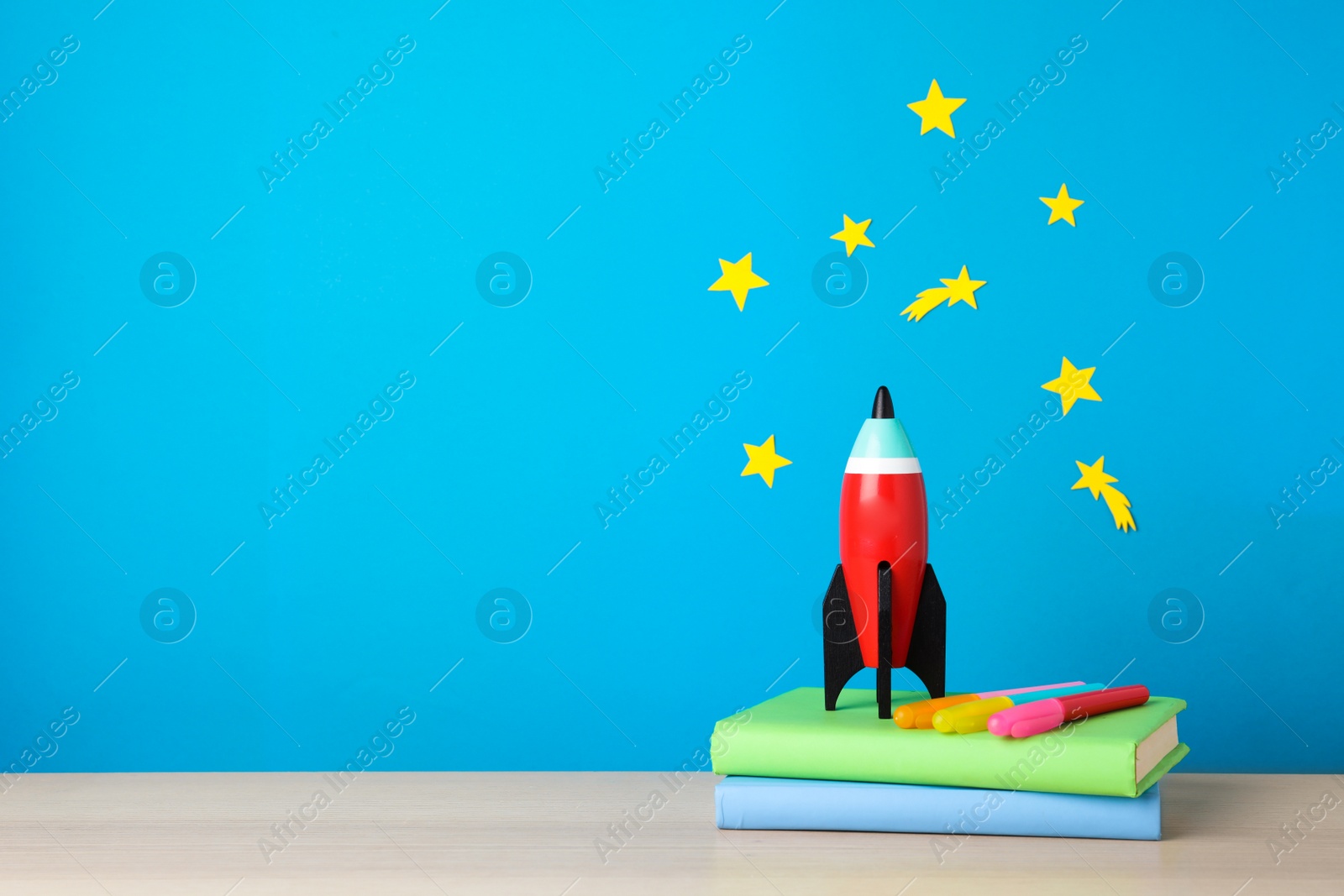 Photo of Bright toy rocket and school supplies on wooden desk. Space for text