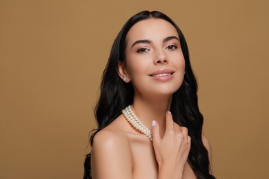 Young woman wearing elegant pearl jewelry on brown background, space for text