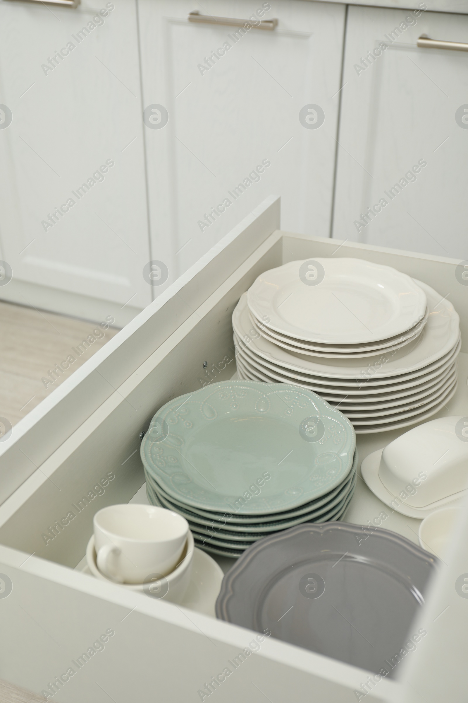 Photo of Clean plates, cups and butter dish in drawer indoors