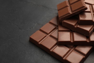 Photo of Delicious milk chocolate on black table, closeup. Space for text