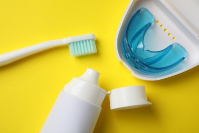 Photo of Toothpaste, brush and dental mouth guard on yellow background, flat lay. Bite correction