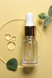 Bottle of cosmetic serum and green leaves on pale yellow background, top view