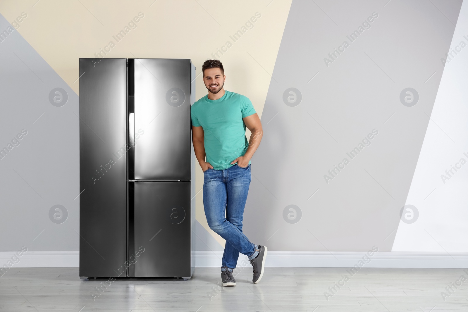 Photo of Happy young man near refrigerator indoors, space for text