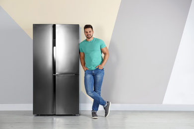 Photo of Happy young man near refrigerator indoors, space for text