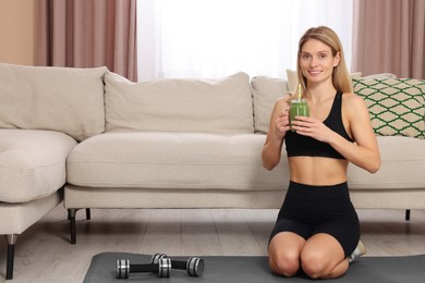 Photo of Young woman in sportswear with mason jar of fresh smoothie at home, space for text
