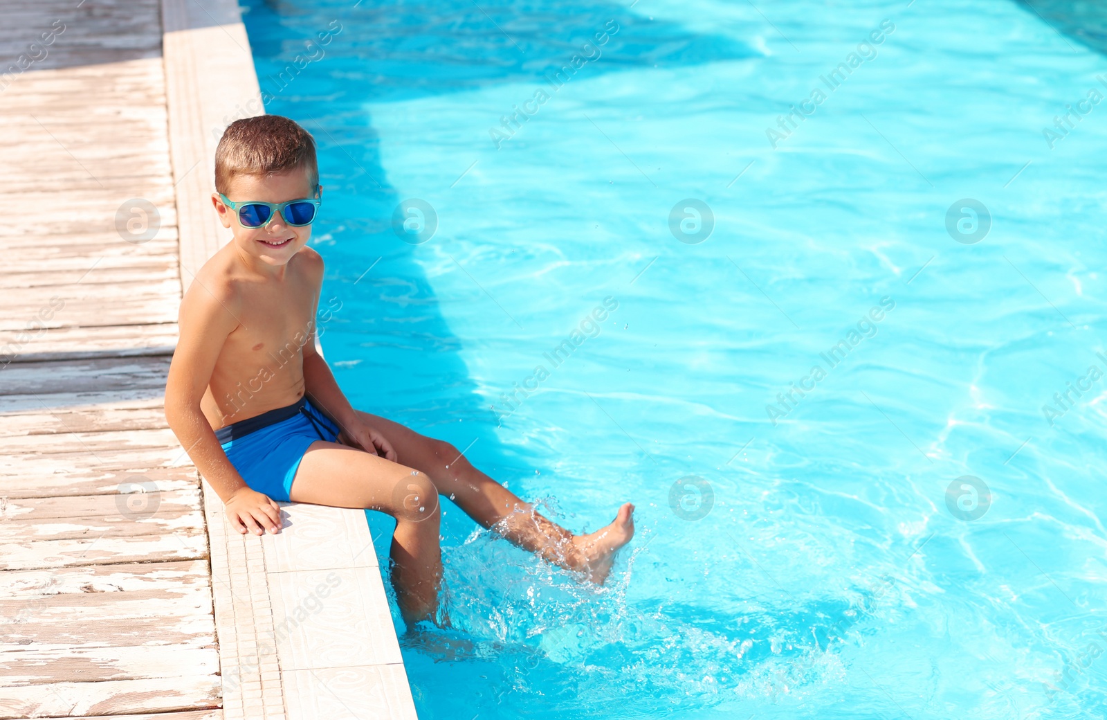 Photo of Cute little boy in sunglasses sitting near swimming pool