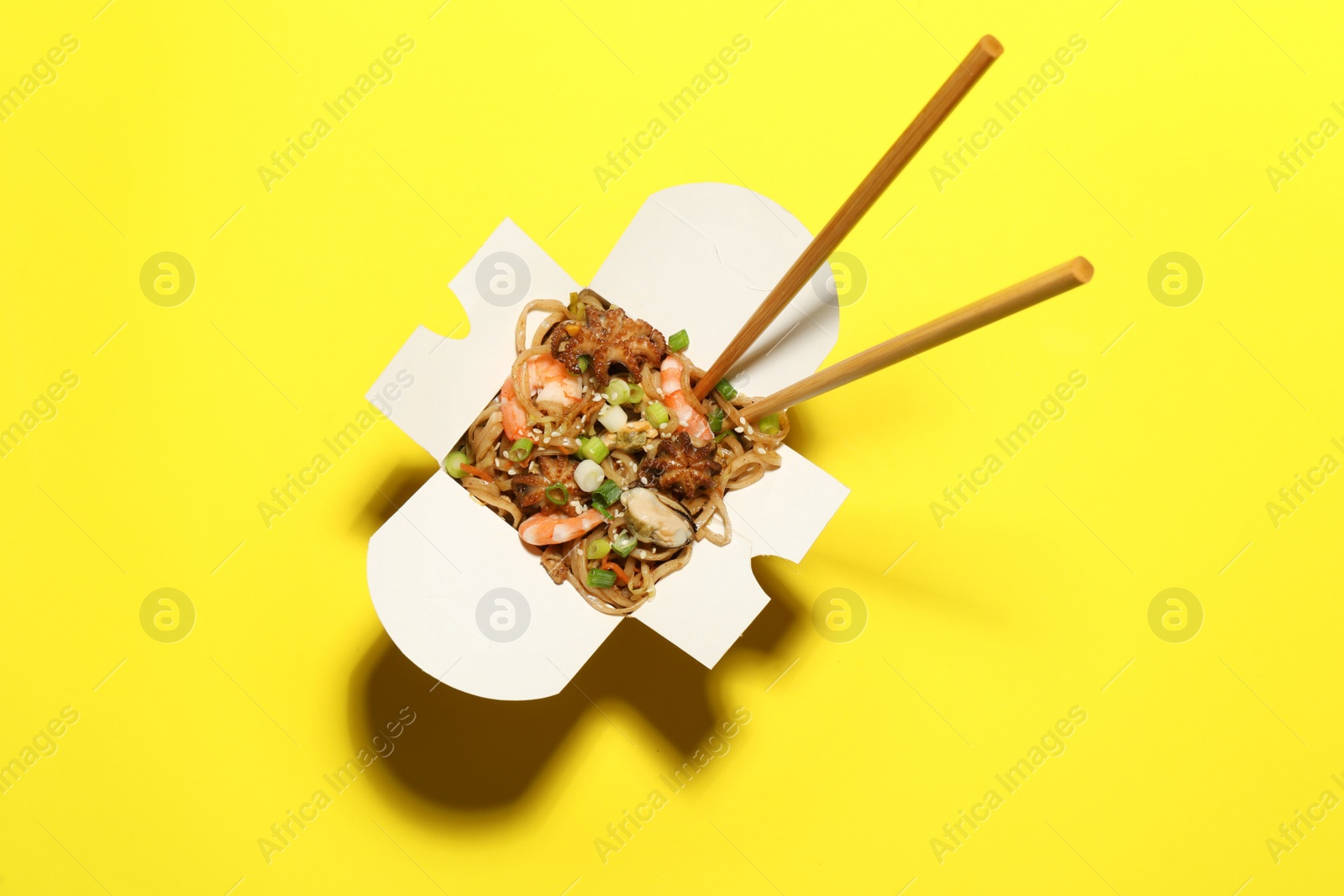 Photo of Box of noodle wok with chopsticks on yellow background, top view