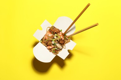 Photo of Box of noodle wok with chopsticks on yellow background, top view