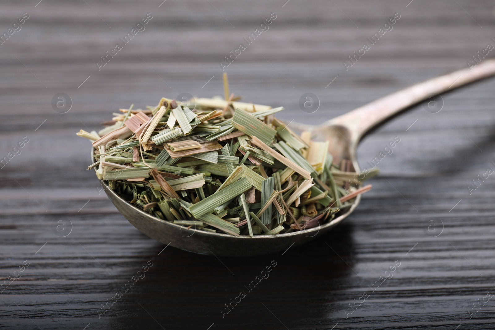 Photo of Metal spoon with aromatic dried lemongrass on wooden table, closeup